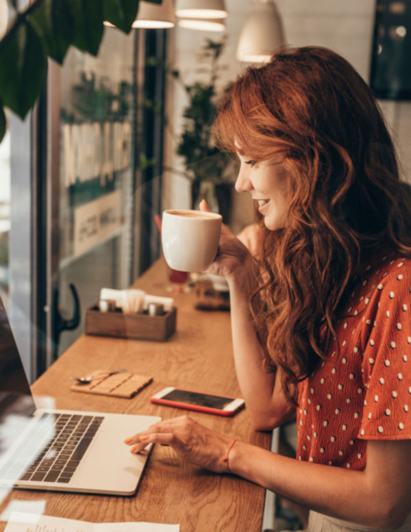 An author smiles at her laptop while holding a coffee cup, pleased with the results of her search engine optimization.